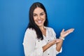 Young hispanic woman standing over blue background pointing aside with hands open palms showing copy space, presenting Royalty Free Stock Photo
