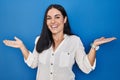 Young hispanic woman standing over blue background smiling showing both hands open palms, presenting and advertising comparison Royalty Free Stock Photo
