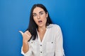 Young hispanic woman standing over blue background surprised pointing with hand finger to the side, open mouth amazed expression Royalty Free Stock Photo