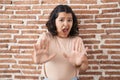 Young hispanic woman standing over bricks wall afraid and terrified with fear expression stop gesture with hands, shouting in Royalty Free Stock Photo