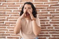 Young hispanic woman standing over bricks wall shouting angry out loud with hands over mouth Royalty Free Stock Photo