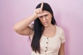 Young hispanic woman standing over pink background making fun of people with fingers on forehead doing loser gesture mocking and Royalty Free Stock Photo