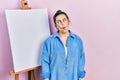 Young hispanic woman standing by painter easel stand making fish face with lips, crazy and comical gesture Royalty Free Stock Photo