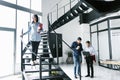 Young hispanic woman standing on the stairs and office colleagues busy working on computer in modern office in Mexico Royalty Free Stock Photo