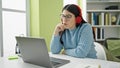 Young hispanic woman student using laptop studying wearing headphones at library university Royalty Free Stock Photo