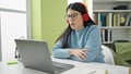 Young hispanic woman student using laptop studying wearing headphones at library university Royalty Free Stock Photo