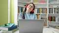 Young hispanic woman student using laptop wearing headphones at library university Royalty Free Stock Photo