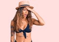 Young hispanic woman with tattoo wearing bikini and summer hat surprised with hand on head for mistake, remember error