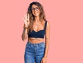 Young hispanic woman with tattoo wearing casual clothes and glasses showing and pointing up with fingers number four while smiling Royalty Free Stock Photo