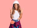 Young hispanic woman with tattoo wearing hardhat and builder clothes shouting with crazy expression doing rock symbol with hands