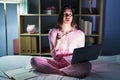 Young hispanic woman using computer laptop on the bed amazed and surprised looking up and pointing with fingers and raised arms Royalty Free Stock Photo