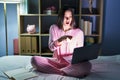 Young hispanic woman using computer laptop on the bed pointing with finger surprised ahead, open mouth amazed expression, Royalty Free Stock Photo