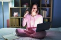 Young hispanic woman using computer laptop on the bed smiling amazed and surprised and pointing up with fingers and raised arms Royalty Free Stock Photo