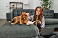 Young hispanic woman using laptop studying sitting on floor with dog at home Royalty Free Stock Photo