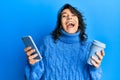 Young hispanic woman using smartphone and drinking a cup of coffee celebrating crazy and amazed for success with open eyes Royalty Free Stock Photo