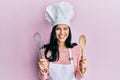 Young hispanic woman wearing baker uniform holding spoon and whisk winking looking at the camera with sexy expression, cheerful Royalty Free Stock Photo