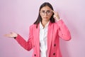 Young hispanic woman wearing business clothes and glasses confused and annoyed with open palm showing copy space and pointing
