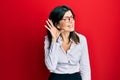 Young hispanic woman wearing business shirt and glasses smiling with hand over ear listening an hearing to rumor or gossip Royalty Free Stock Photo