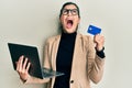 Young hispanic woman wearing business style holding laptop and credit card angry and mad screaming frustrated and furious, Royalty Free Stock Photo