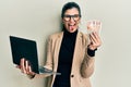 Young hispanic woman wearing business style holding laptop and united kingdom pounds sticking tongue out happy with funny
