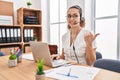 Young hispanic woman wearing call center agent headset at the office smiling with happy face looking and pointing to the side with Royalty Free Stock Photo