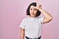 Young hispanic woman wearing casual white t shirt over pink background making fun of people with fingers on forehead doing loser Royalty Free Stock Photo