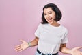 Young hispanic woman wearing casual white t shirt over pink background smiling cheerful with open arms as friendly welcome, Royalty Free Stock Photo