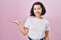Young hispanic woman wearing casual white t shirt over pink background smiling cheerful presenting and pointing with palm of hand Royalty Free Stock Photo