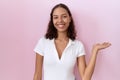 Young hispanic woman wearing casual white t shirt smiling cheerful presenting and pointing with palm of hand looking at the camera Royalty Free Stock Photo