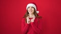 Young hispanic woman wearing christmas hat crossing fingers for lucky over isolated red background