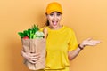 Young hispanic woman wearing courier uniform with groceries from supermarket celebrating achievement with happy smile and winner Royalty Free Stock Photo