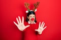 Young hispanic woman wearing deer christmas hat and red nose afraid and terrified with fear expression stop gesture with hands, Royalty Free Stock Photo