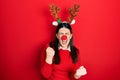 Young hispanic woman wearing deer christmas hat and red nose celebrating surprised and amazed for success with arms raised and Royalty Free Stock Photo