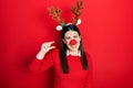 Young hispanic woman wearing deer christmas hat and red nose smiling and confident gesturing with hand doing small size sign with Royalty Free Stock Photo