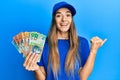 Young hispanic woman wearing delivery uniform and cap holding australian dollars pointing thumb up to the side smiling happy with Royalty Free Stock Photo