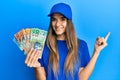 Young hispanic woman wearing delivery uniform and cap holding australian dollars smiling happy pointing with hand and finger to Royalty Free Stock Photo