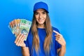 Young hispanic woman wearing delivery uniform and cap holding australian dollars smiling happy pointing with hand and finger Royalty Free Stock Photo