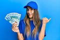 Young hispanic woman wearing delivery uniform and cap holding 20 hong kong dollars pointing thumb up to the side smiling happy Royalty Free Stock Photo
