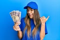 Young hispanic woman wearing delivery uniform and cap holding japanese yuan pointing thumb up to the side smiling happy with open Royalty Free Stock Photo