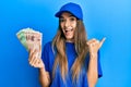 Young hispanic woman wearing delivery uniform and cap holding south korean won pointing thumb up to the side smiling happy with Royalty Free Stock Photo