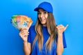 Young hispanic woman wearing delivery uniform and cap holding swiss franc pointing thumb up to the side smiling happy with open Royalty Free Stock Photo