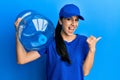 Young hispanic woman wearing delivery uniform holding water carafe pointing thumb up to the side smiling happy with open mouth Royalty Free Stock Photo