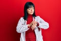 Young hispanic woman wearing doctor uniform and stethoscope checking the time on wrist watch, relaxed and confident Royalty Free Stock Photo