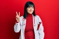 Young hispanic woman wearing doctor uniform and stethoscope smiling looking to the camera showing fingers doing victory sign Royalty Free Stock Photo