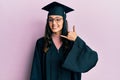Young hispanic woman wearing graduation cap and ceremony robe smiling doing phone gesture with hand and fingers like talking on Royalty Free Stock Photo