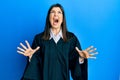 Young hispanic woman wearing judge uniform crazy and mad shouting and yelling with aggressive expression and arms raised