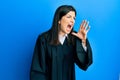 Young hispanic woman wearing judge uniform shouting and screaming loud to side with hand on mouth