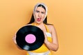 Young hispanic woman wearing pin up style holding vinyl disc in shock face, looking skeptical and sarcastic, surprised with open