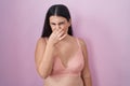 Young hispanic woman wearing pink bra smelling something stinky and disgusting, intolerable smell, holding breath with fingers on Royalty Free Stock Photo