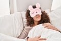 Young hispanic woman wearing sleepmask sleeping on bed at bedroom